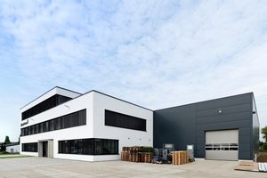  Die weiße Fassade des Bürogebäudes bildet einen Kontrast zur dunkelgrauen Farbe der Produktionshalle. 