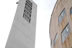  Der instandgesetzte Turm. Daneben das Kirchenschiff, das aus finanziellen Gründen zu einem späteren Zeitpunkt instandgesetzt werden soll. Der rötliche Anstrich geht auf eine Instandsetzung in den 80er Jahren zurück. Damit sollte seinerzeit die ursprünglich rötlich-graue Tönung der früheren Sichtbetonfassade aus Ziegelsplitt wiederhergestellt werden.  