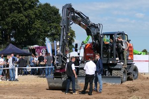  Ulrich Recknagel (Bildmitte) von Holp erläutert zwei Interessenten die Funktionsweise des Drehantriebs Rototop, während andere Besucher die Bedienelemente des Atlas-Baggers 175 WSR blue inspizieren. 