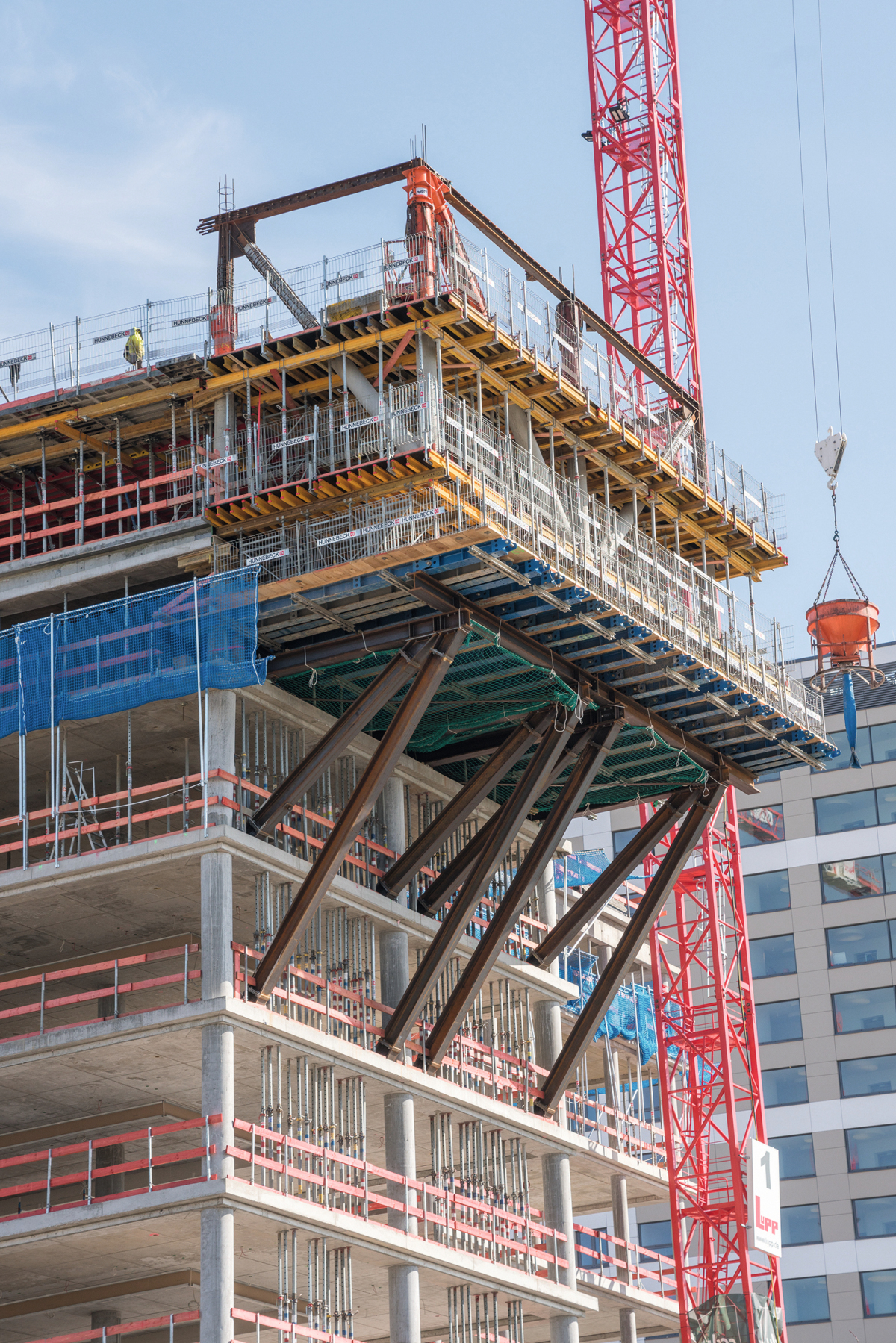 Die beiden auskragenden, gedrehten Gebäudebereiche wurden mit einer rückverankerten Konsollösung aus Stahlträgern realisiert. Hünnebeck steuerte den Aufbau der temporären Plattform bei: Träger aus dem modularen Baukastensystem Infra-Kit sowie Schwerlastra