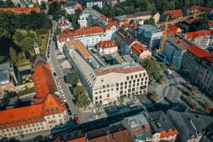  Das Hotel- und Geschäftsgebäude bildet mit seiner außergewöhnlichen Dachform und Fassadengestaltung einen markanten Stadtbaustein am Pasinger Marienplatz. 