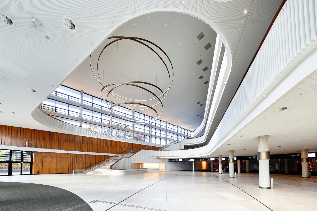 Das Foyer bildet das Herz des Gebäudes. Im Zentrum der 4-geschossigen Halle befindet sich ein an speziellen Deckentraversen befestigte 3,4 Tonnen schwere Pendelleuchte.