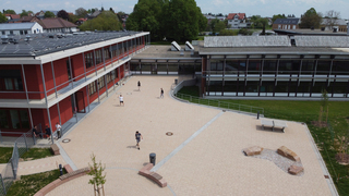 Der Pausenhof, der bisher auf der Vorderseite des alten Schulgebäudes (r.) angesiedelt war, wurde auf die Gebäuderückseite verlegt. Hier entstand eine Schulhoffläche, die den Hauptausgang aus dem Altbau als auch den Notausgang des Neubaus (l.) erschließt.