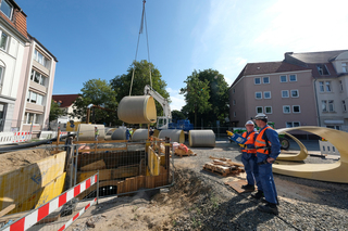 Die GFK-Rohre werden mit einem Kran in die Baugrube abgelassen und von dort mit einem speziellen Fahrwagen in die Lutter-Verrohrung eingefahren. Alexander Garen (Umweltbetrieb der Stadt Bielefeld, rechts) und Prüfingenieur Guido Heidbrink (Güteschutz Kana