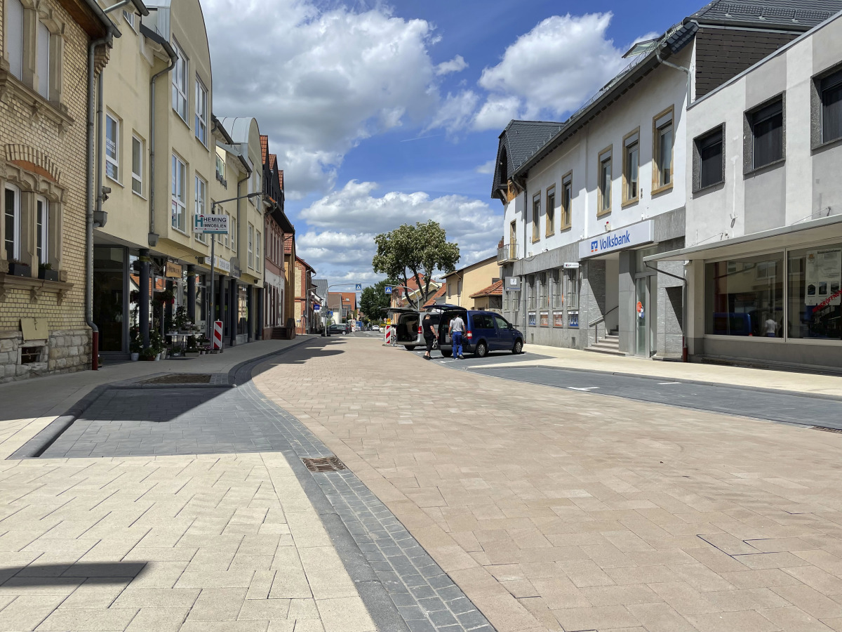 Das oberflächenbehandelte Betonpflaster wirkt deutlich schöner als die ehemals asphaltierte Fläche. Die farbliche Trennung von Fahrbahn, Gehweg und Parkstreifen strukturiert den barrierefrei angelegten Straßenraum.