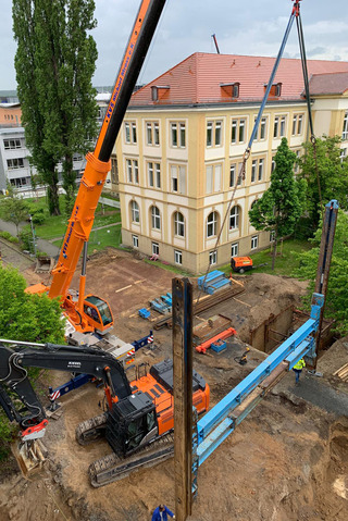 Die vor Ort vormontierten Linearverbauträger mit Laufwagen werden in den Voraushub der Baugrube eingestellt.