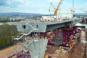  Im Bau befindliche Schiersteiner Brücke. Der Brückenabschnitt wird an Land auf der Rheininsel Rettbergsaue vormontiert und später in Längsrichtung Rhein in Endlage verschoben. So kann der Schiffsverkehr während der Bauphase ungehindert fließen. © Max Bögl Stahl- und Anlagenbau 