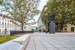  Der Platz wurde mit großformatigen Betonplatten gepflastert. Dabei schaffen die breiten Betonblöcke zum Sitzen eine erlebbare Raumkante, an die sich das Grün zur Straße hin anschließt. 