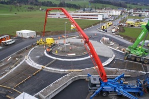  2 Der Beton für die Fahrbahn wird vom Verteilermast einer stationär aufgebauten Betonpumpe (unten rechts) kontinuierlich vor den Kreiselfertiger geschüttet, der hier nach nur 90 Minuten schon die Hälfte der Betonfahrbahn des Kreisverkehrs fertiggestellt hat 