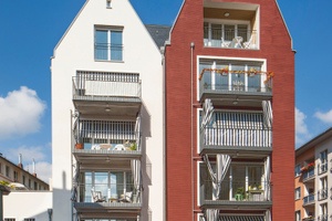  Die architektonische Eigenständigkeit der beiden Gebäudehälften wird durch die unterschiedlichen Putzarten und -farben unterstrichen, weiß und rot. 